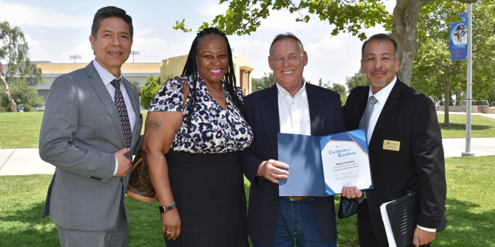 Wayne Hamilton smiling and holding his award certificate, flanked by Dr. Vargas and other members of district administration